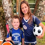 A girl holding a soccer ball beside her younger brother with a T-ball bat